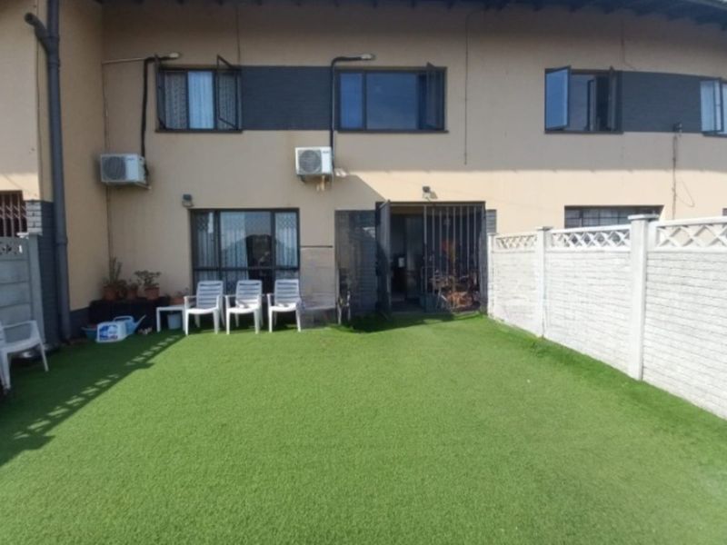 Rear view of the townhouse featuring a private artificial grass garden, secure boundary walling, and exterior air conditioning units.