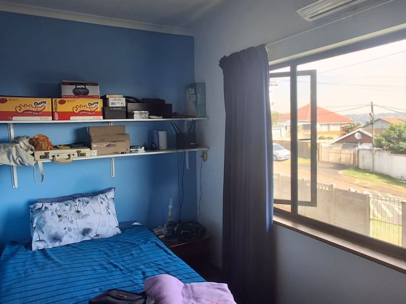 A bedroom featuring blue walls, wall-mounted shelving, a split-system air conditioner, and a large window with views of the street.