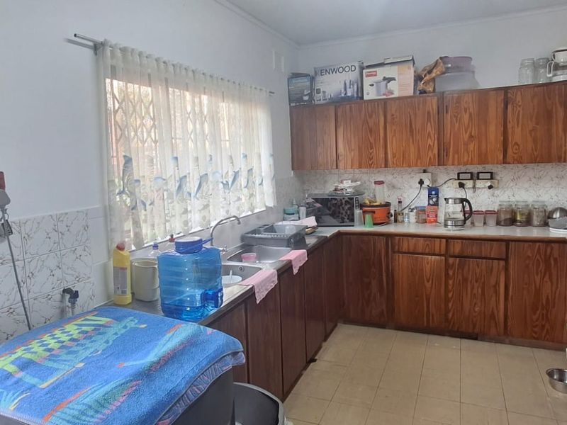 A functional kitchen featuring wooden cabinetry, a double basin sink, and tiled backsplash, offering a dated aesthetic ready for modernization.