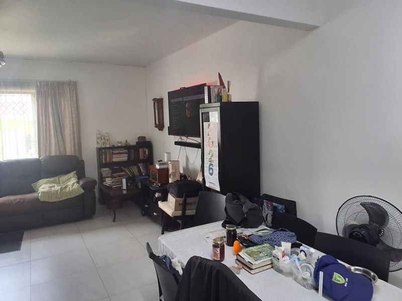 Open-plan living and dining area featuring tiled flooring, a ceiling fan, and large windows with security bars.