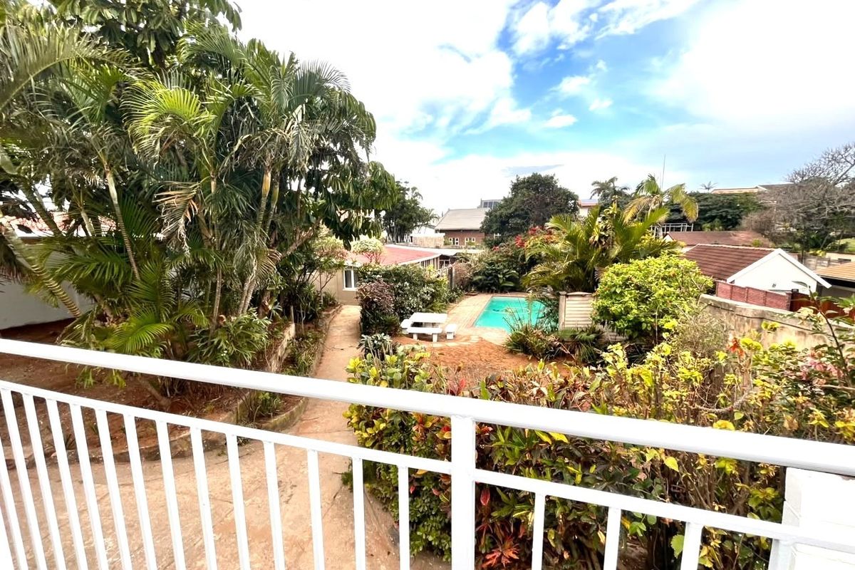Elevated view of a rear garden featuring a swimming pool, paved pathways, and established tropical landscaping viewed from a balcony.