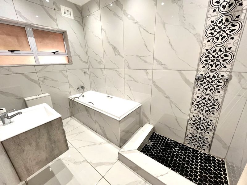 Modern bathroom featuring a built-in bathtub, separate walk-in shower with decorative tiling, vanity basin, and contemporary marble-look wall finishes.