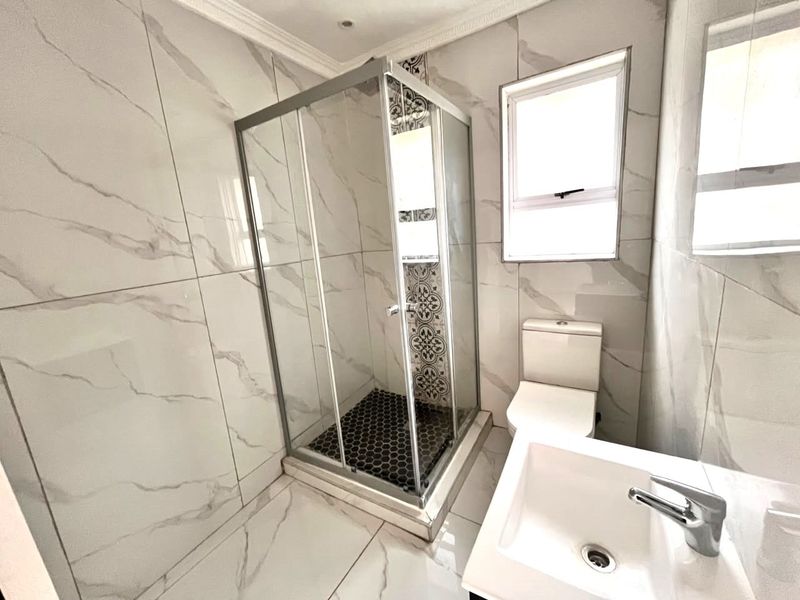 Modern bathroom featuring a glass shower enclosure, white vanity basin with mixer tap, toilet, and contemporary marble-look wall tiles.