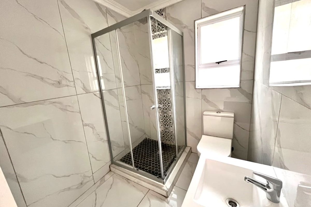 Modern bathroom featuring a glass shower enclosure, white vanity basin with mixer tap, toilet, and contemporary marble-look wall tiles.