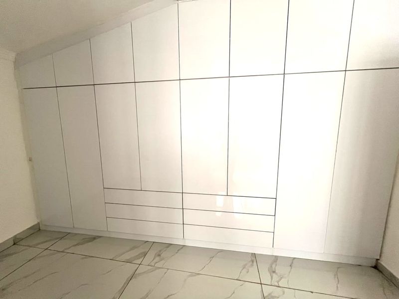 A clean, modern bedroom featuring extensive white built-in floor-to-ceiling cabinetry and large-format marble-look floor tiles.