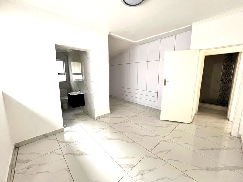 Spacious bedroom featuring modern marble-look porcelain floor tiles, extensive built-in cabinetry, and an adjoining en-suite bathroom.