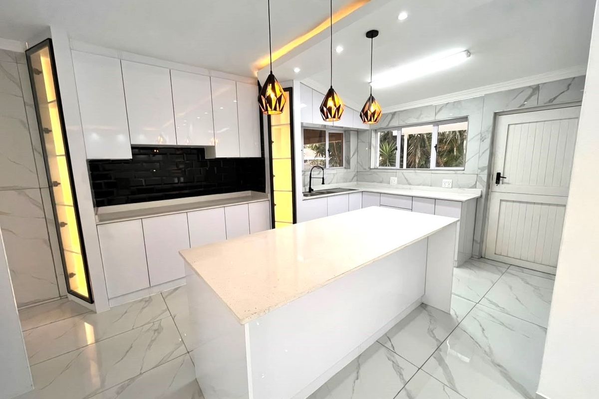 Modern, renovated kitchen featuring a central island, quartz countertops, sleek white cabinetry, black subway tile backsplash, and elegant marble-look floor tiles.