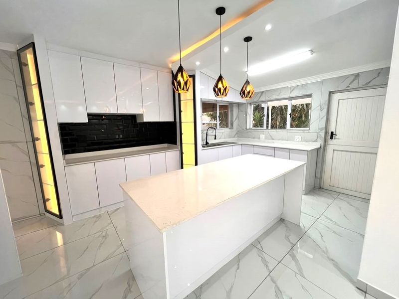 Modern, renovated kitchen featuring a central island, quartz countertops, sleek white cabinetry, black subway tile backsplash, and elegant marble-look floor tiles.
