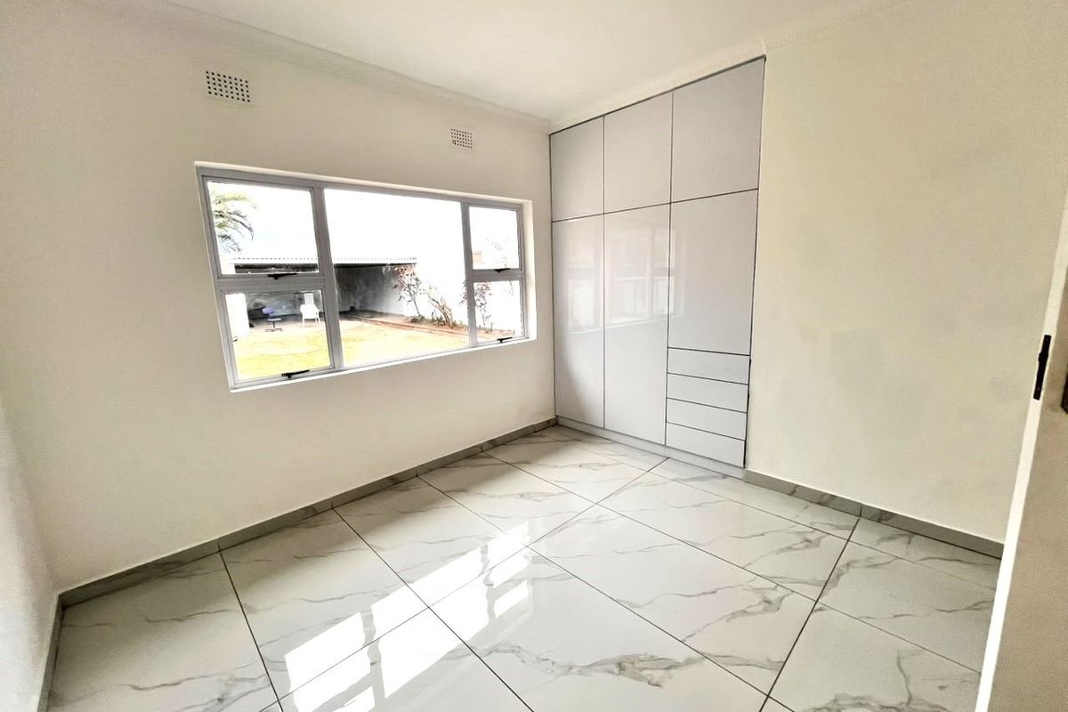 A bright, modern bedroom featuring high-gloss built-in cupboards and polished marble-look floor tiles, offering a clean and contemporary living space.