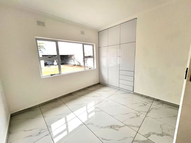 A bright, modern bedroom featuring high-gloss built-in cupboards and polished marble-look floor tiles, offering a clean and contemporary living space.