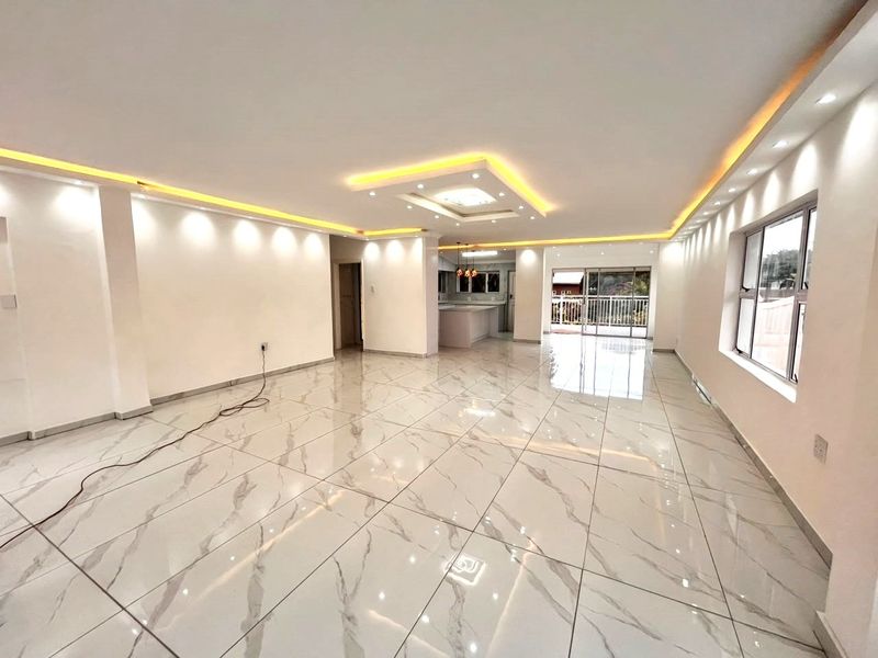 Spacious open-plan living area featuring modern marble-look floor tiles, recessed cove lighting, and seamless flow to the kitchen and outdoor patio area.