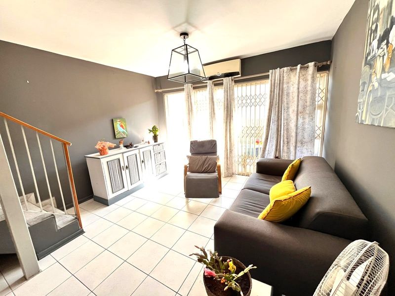 A living room featuring tiled flooring, a staircase with a wooden handrail, and a wall-mounted air conditioning unit, leading to a secure patio entrance.