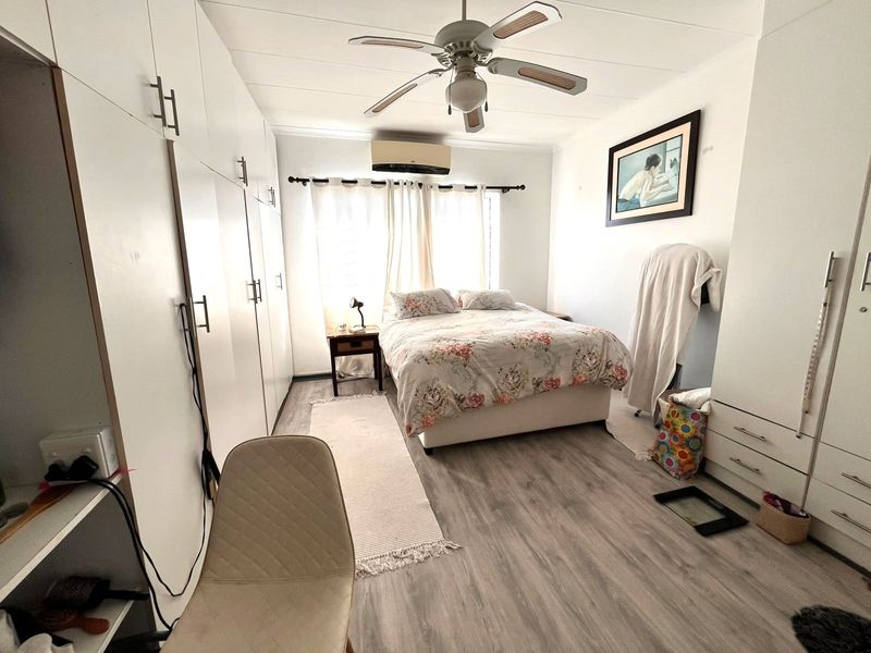 A well-lit bedroom featuring extensive built-in cupboards, modern laminate flooring, a ceiling fan, and a wall-mounted air conditioning unit.