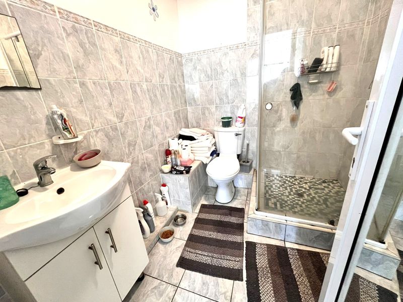 A functional bathroom featuring a vanity basin, toilet, and a glass-enclosed shower with full-height wall tiling.