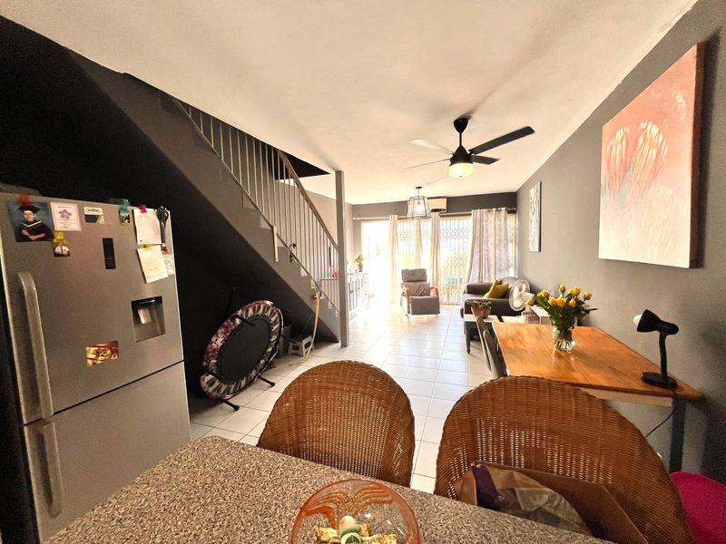 Open-plan living and dining area featuring tiled flooring, a central staircase with metal balustrade, and sliding glass doors leading to the exterior.