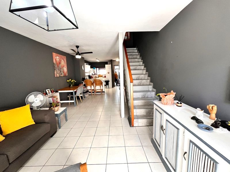 Open-plan living and dining area featuring tiled flooring, a central staircase, and a connected kitchen space with modern dark wall accents.