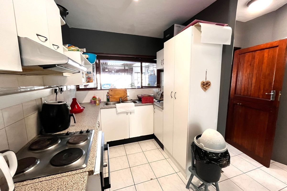 A functional kitchen featuring white cabinetry, laminate countertops, an electric hob with extractor fan, and tiled flooring with direct access to an adjacent room.