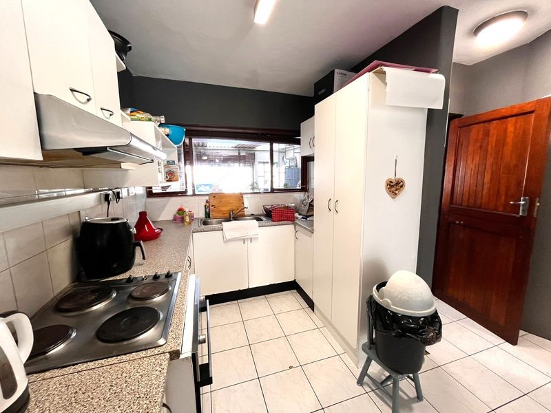A functional kitchen featuring white cabinetry, laminate countertops, an electric hob with extractor fan, and tiled flooring with direct access to an adjacent room.