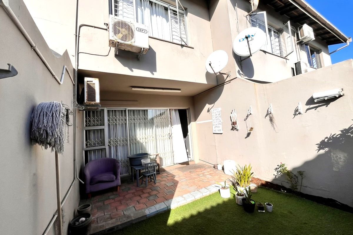 Rear exterior view of the townhouse featuring a paved patio area, artificial lawn, and secure sliding door access.