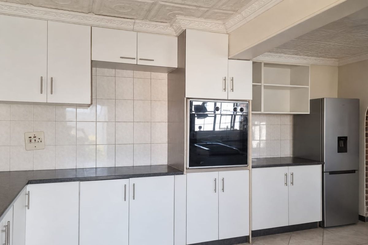 A functional kitchen featuring white cabinetry, dark laminate countertops, tiled backsplash, and a built-in oven, complemented by decorative ceiling detailing.