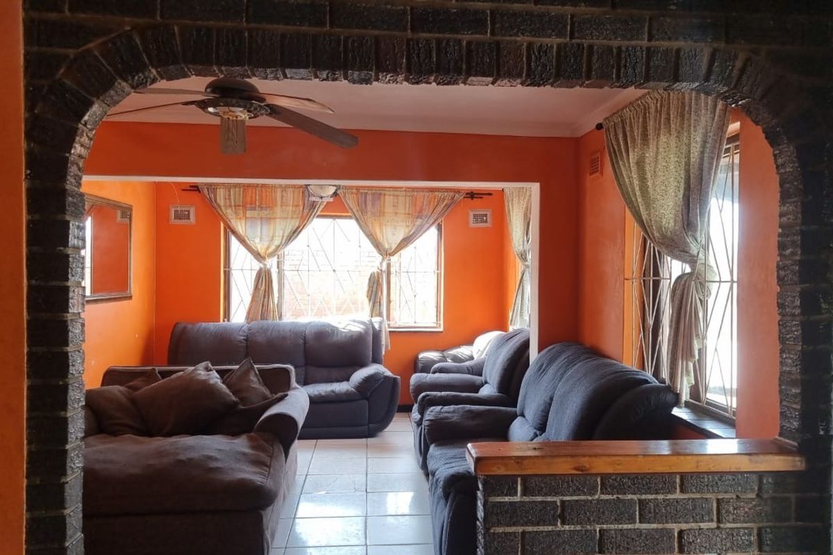 A living room featuring a distinctive brick archway, tiled flooring, and a ceiling fan, with large windows fitted with security bars.
