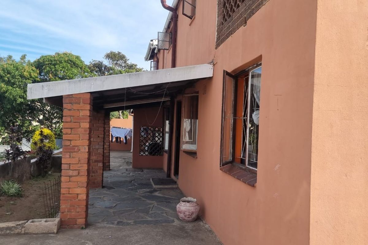 A rear exterior view of the house featuring a covered patio area with brick pillars and paved flooring.