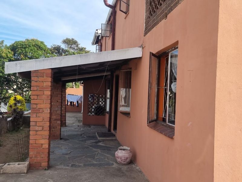 A rear exterior view of the house featuring a covered patio area with brick pillars and paved flooring.