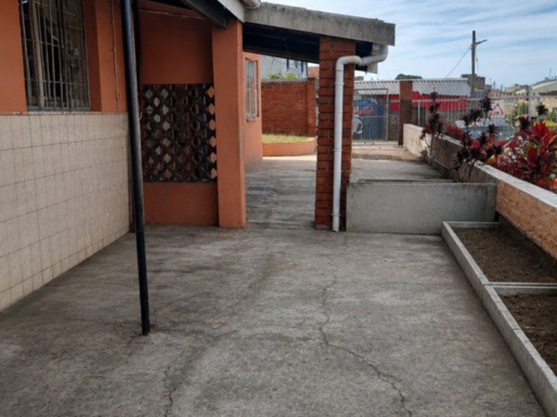Rear exterior area featuring a concrete patio, brick support pillars, and raised planter boxes, showing signs of wear and surface cracking.
