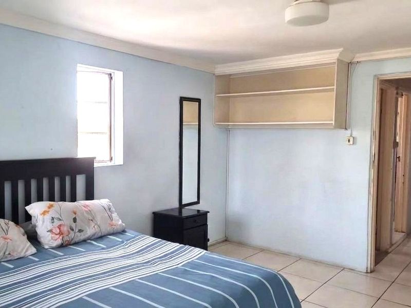 A bedroom featuring tiled flooring, built-in wall shelving, and cornicing, with an adjoining doorway leading to another area of the home.