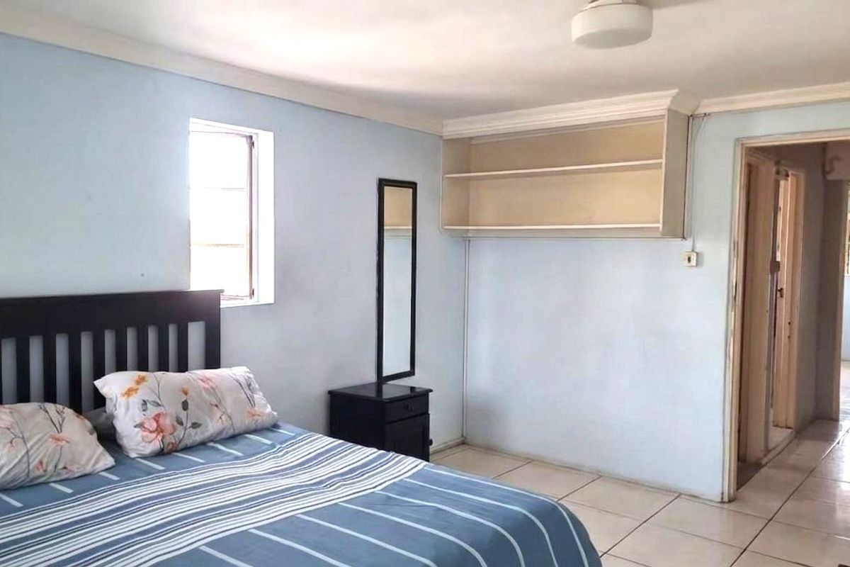 A bedroom featuring tiled flooring, built-in wall shelving, and cornicing, with an adjoining doorway leading to another area of the home.