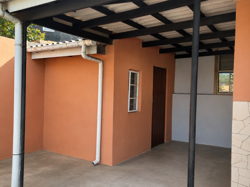 A covered outdoor patio area featuring exposed beams, concrete flooring, and direct access to the main entrance through a timber door.