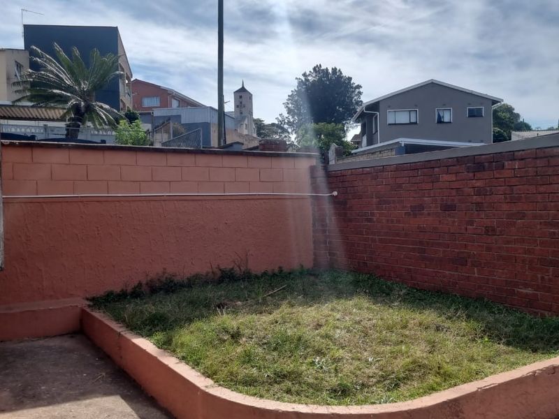 A rear outdoor area featuring a grassed section enclosed by brick and concrete boundary walls.