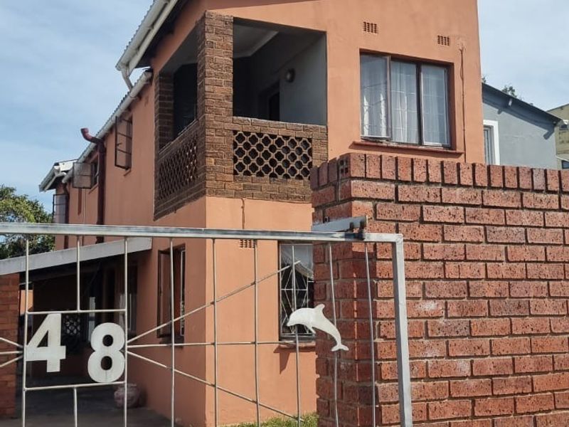 Front view of a two-story residential property featuring a brick boundary wall, metal security gate, and an upper-level balcony.