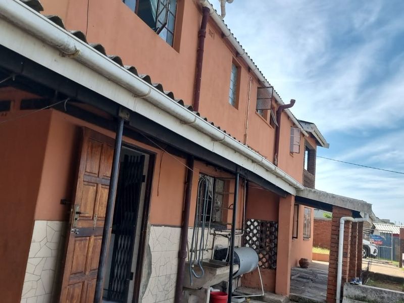 Rear elevation of a two-story house featuring a utility sink, security gate, and external drainage systems, showing signs of wear on the facade.