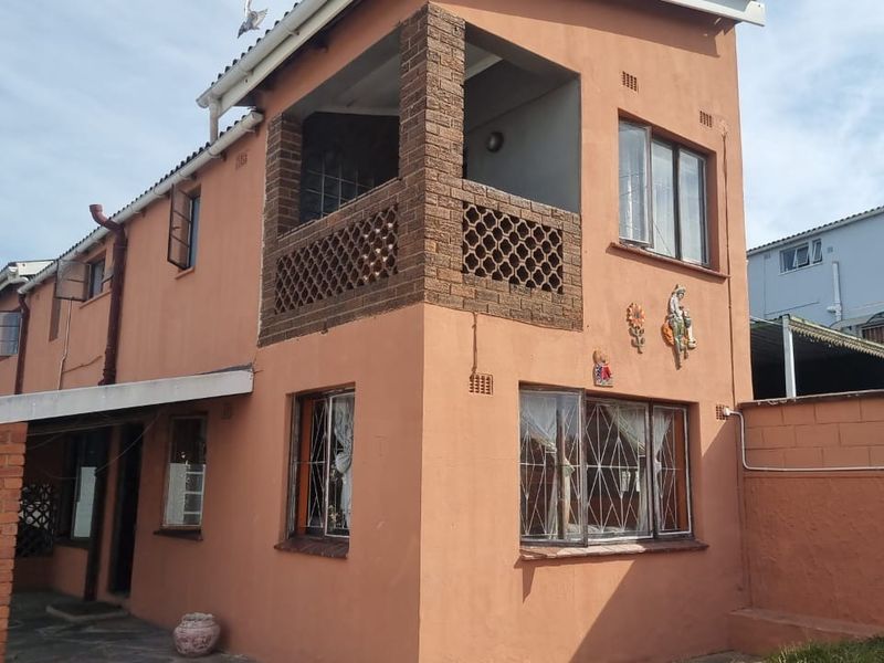 Two-story residential exterior featuring a brick balcony, security bars on windows, and a covered patio area with brick pillars.