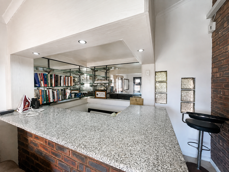A built-in home bar featuring a granite countertop, brick base, mirrored shelving, and decorative glass block accents, creating a functional entertainment space.