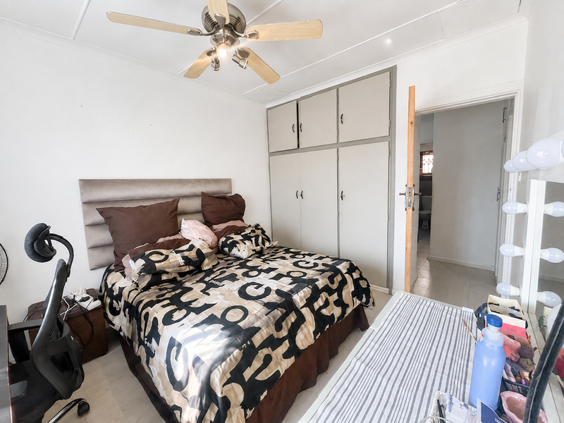 A functional bedroom featuring built-in cupboards, a ceiling fan, and tiled flooring, with direct access to an adjoining bathroom.