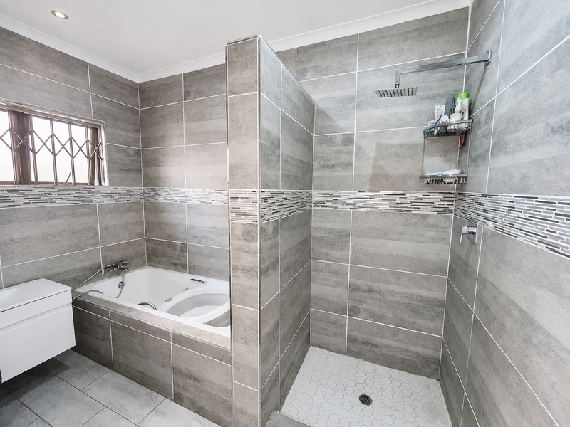 Modern bathroom featuring a built-in bathtub and a separate walk-in shower with grey tiled walls and a mosaic accent border.