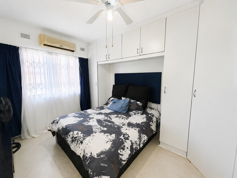 A bedroom featuring built-in white cabinetry, a ceiling fan, and a wall-mounted air conditioning unit, providing functional storage and climate control.