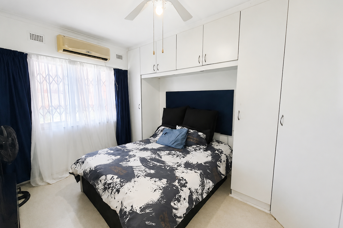 A bedroom featuring built-in white cabinetry, a ceiling fan, and a wall-mounted air conditioning unit, providing functional storage and climate control.