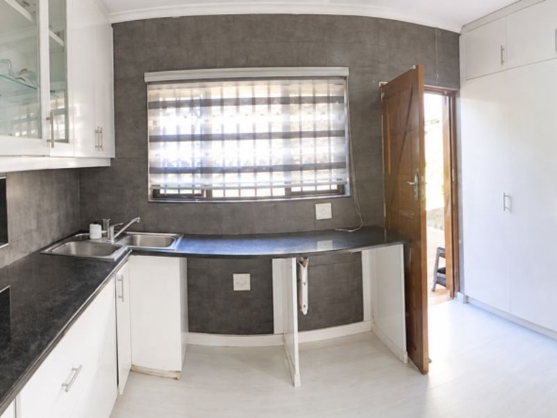 Modern kitchen featuring white cabinetry, dark countertops, integrated appliances, and a window with security bars, providing a functional and clean workspace.