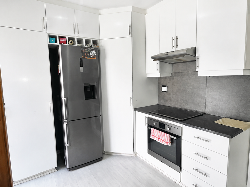Modern kitchen featuring white cabinetry, dark stone countertops, integrated oven, electric hob, and a stainless steel extractor fan.