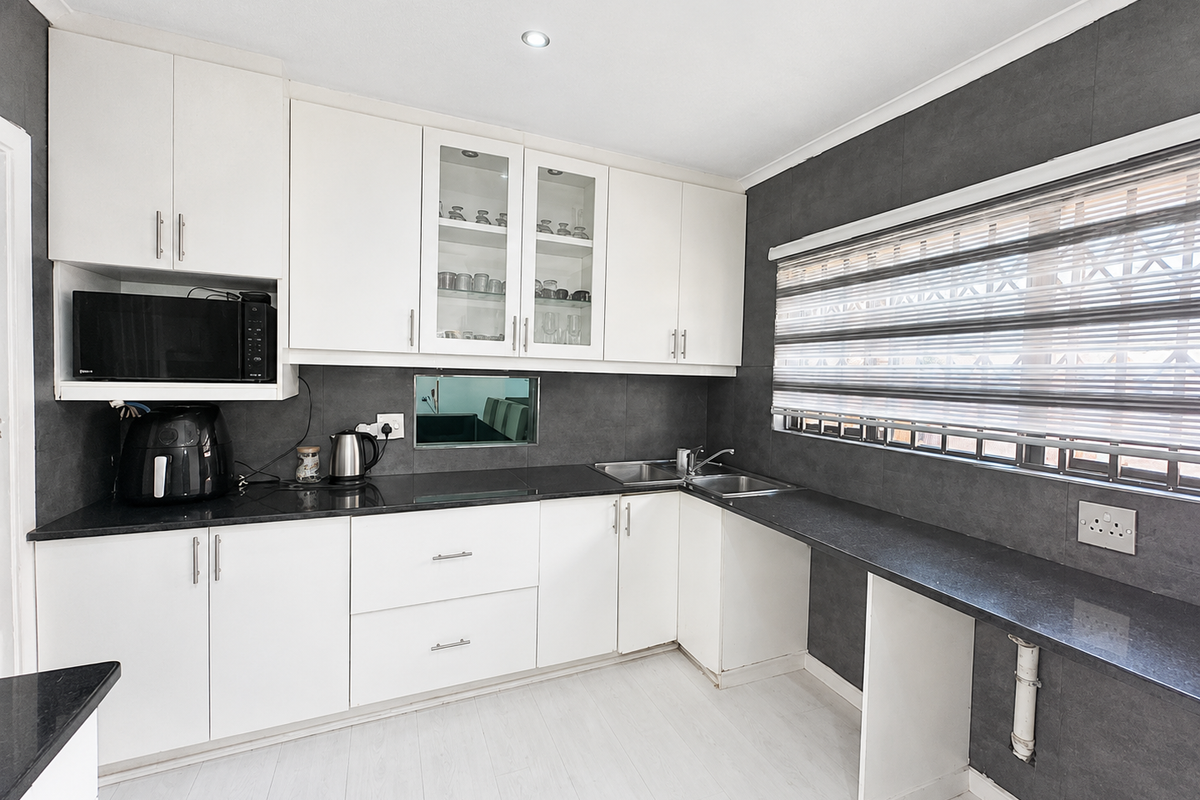 Modern kitchen featuring white cabinetry, dark granite countertops, double basin sink, and built-in microwave with integrated lighting.
