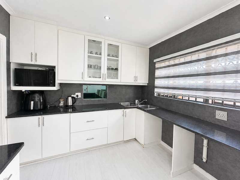 Modern kitchen featuring white cabinetry, dark granite countertops, double basin sink, and built-in microwave with integrated lighting.