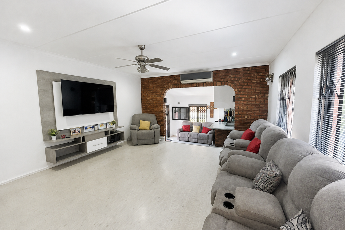 Spacious living room featuring an exposed brick accent wall, ceiling fan, split-system air conditioning, and a custom built-in media unit.