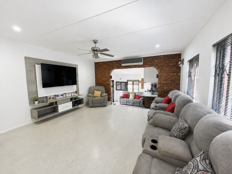 Spacious living room featuring an exposed brick accent wall, ceiling fan, split-system air conditioning, and a custom built-in media unit.
