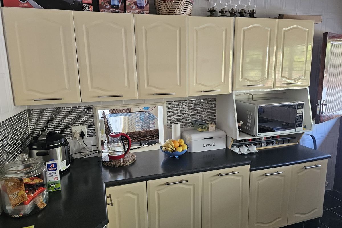 A functional kitchen featuring cream-colored cabinetry, dark laminate countertops, and a decorative tiled backsplash with a built-in microwave shelf.