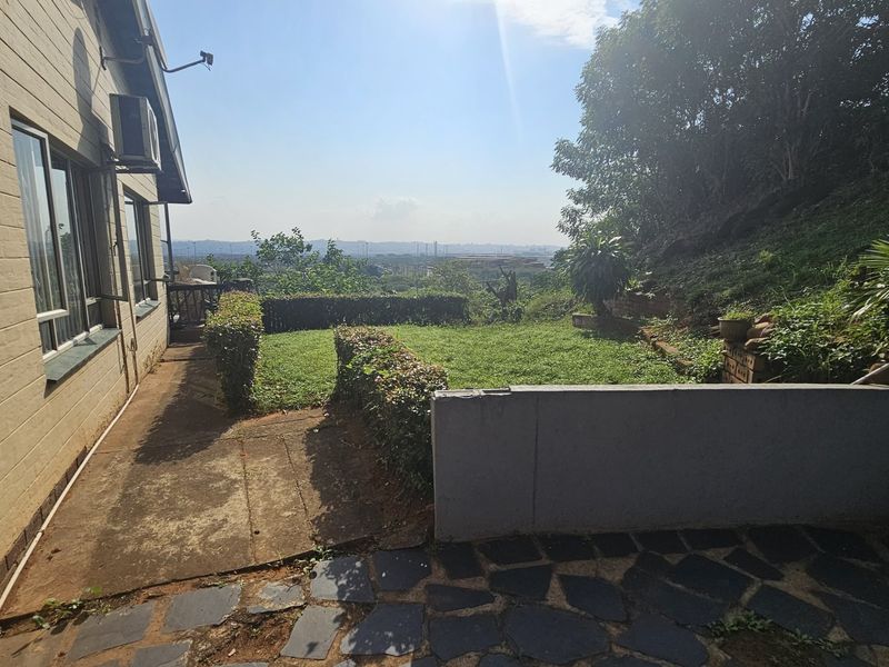 Rear exterior view featuring a lawn, concrete paving, and a retaining wall with distant landscape views.