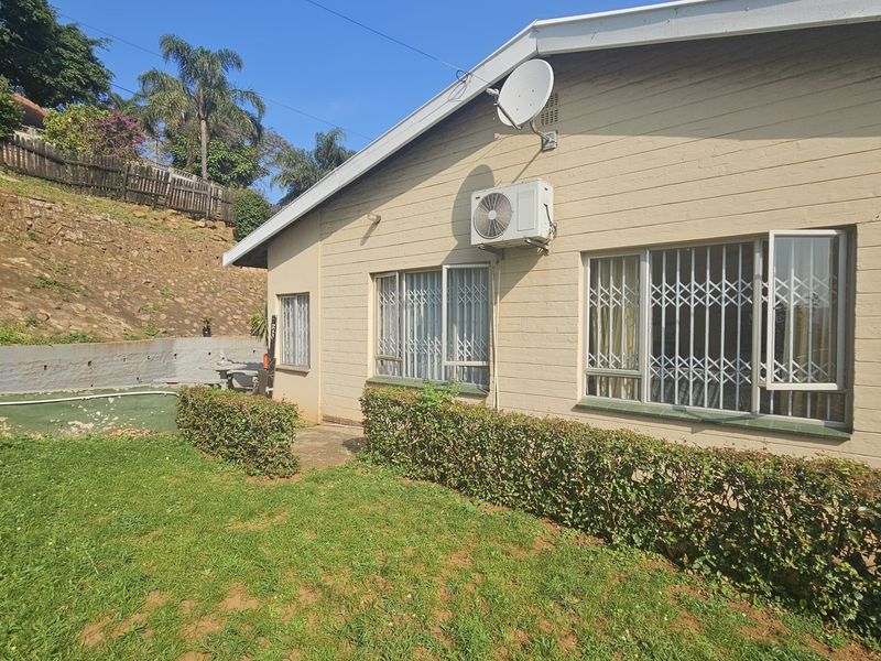 Rear exterior view of the house featuring a lawn, retaining wall, and security bars on the windows with an installed air conditioning unit.