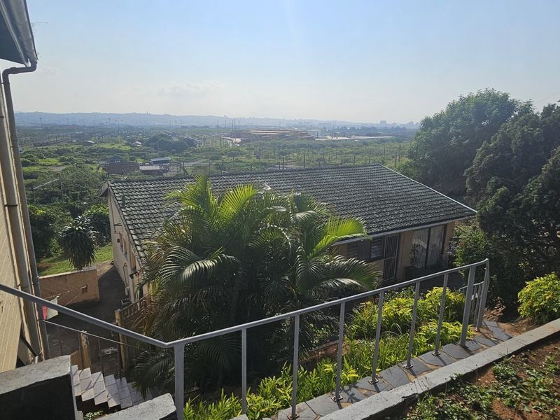 An elevated rear view of the property showing the tiled roof, surrounding garden area, and distant landscape views.